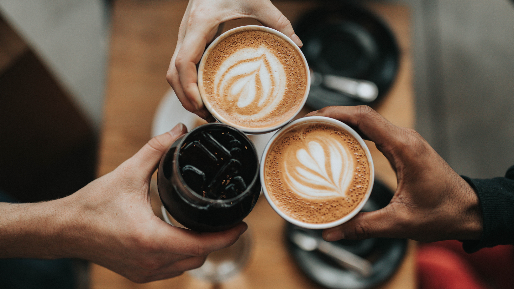 hands holding coffees, lattes and iced drinks